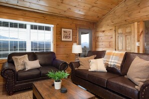 A cozy room with two leather sofas, a wooden coffee table, and a window with blinds.
