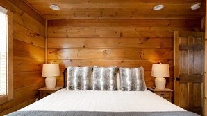 Ett sovrum i en stuga med träpanel, en stor säng, två sänglampor och en trädörr.