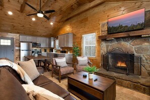 Interior acogedor de una cabaña con chimenea, paredes de madera, zona de comedor y televisor montado en la pared.