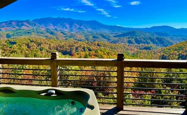 A hot tub on a wooden deck with a view of a mountainous landscape.