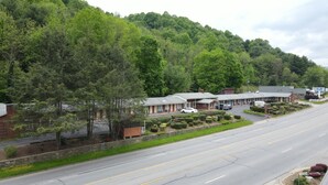 A motel with a row of rooms, a parking lot, and a road leading to a hill. - Parkway Inn (Waynesville)