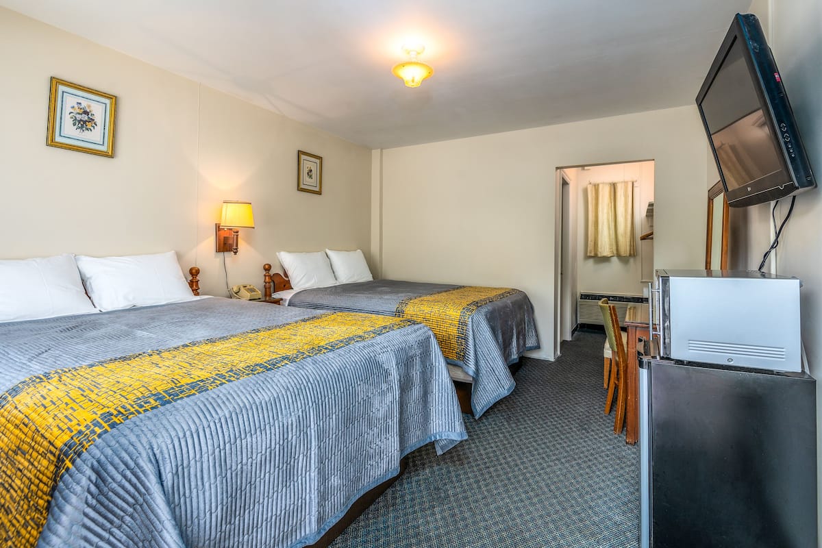 A hotel room with two beds, a desk, a television, and a lamp.