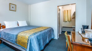 A hotel room with a bed, a wooden chair, a table with a coffee maker, and a picture on the wall. - Parkway Inn (Waynesville)