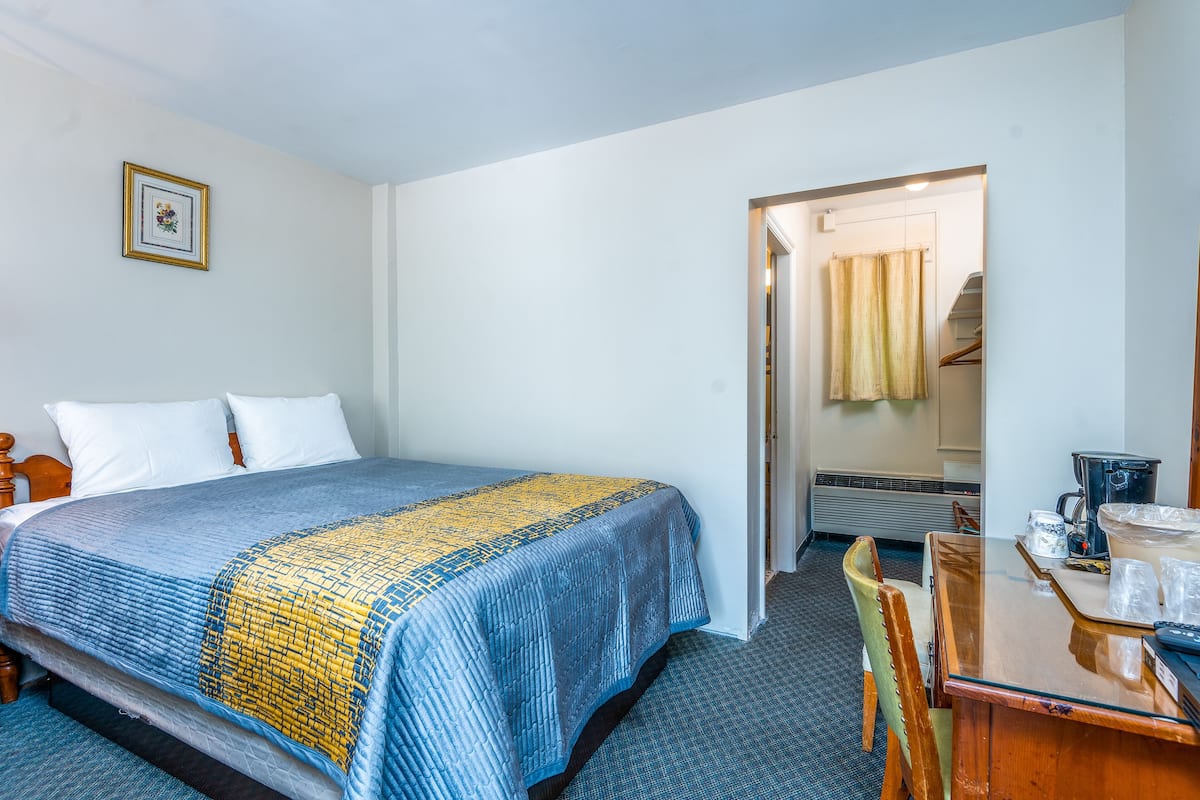 A hotel room with a bed, a wooden chair, a table with a coffee maker, and a picture on the wall.