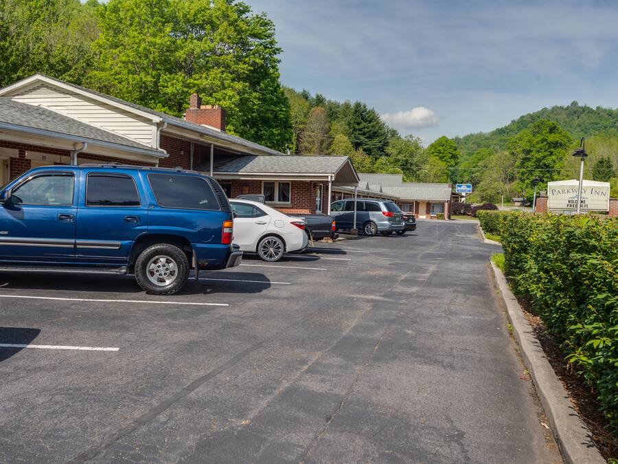 A parking lot with several cars, a building with a sign for Parkway Inn, and a view of a forested hill in the background.