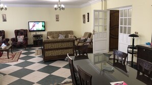 A living room with a checkered floor, a television, floral armchairs, a sofa, and a dining table with chairs. - A Cosy Three Bedrooms  Apartment in Degla, Maadi ,Cairo, Egypt. (Maadi)