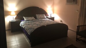 A bedroom with a bed, two bedside tables with lamps, a wall-mounted air conditioner, and a chair. - A Cosy Three Bedrooms  Apartment in Degla, Maadi ,Cairo, Egypt. (Maadi)