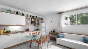 Una cucina moderna con mobili bianchi, un tavolo da pranzo in vetro e un divano bianco con cuscini blu.