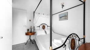 Un letto a baldacchino con biancheria bianca, un comodino con una lampada e un quadro incorniciato appeso al muro.