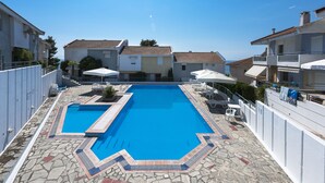 Una piscina con bordo in pietra, circondata da edifici bianchi con tetti in tegole rosse.