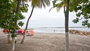 Ein Strand mit Palmen, roten und blauen Zelten und einer felsigen Küste.