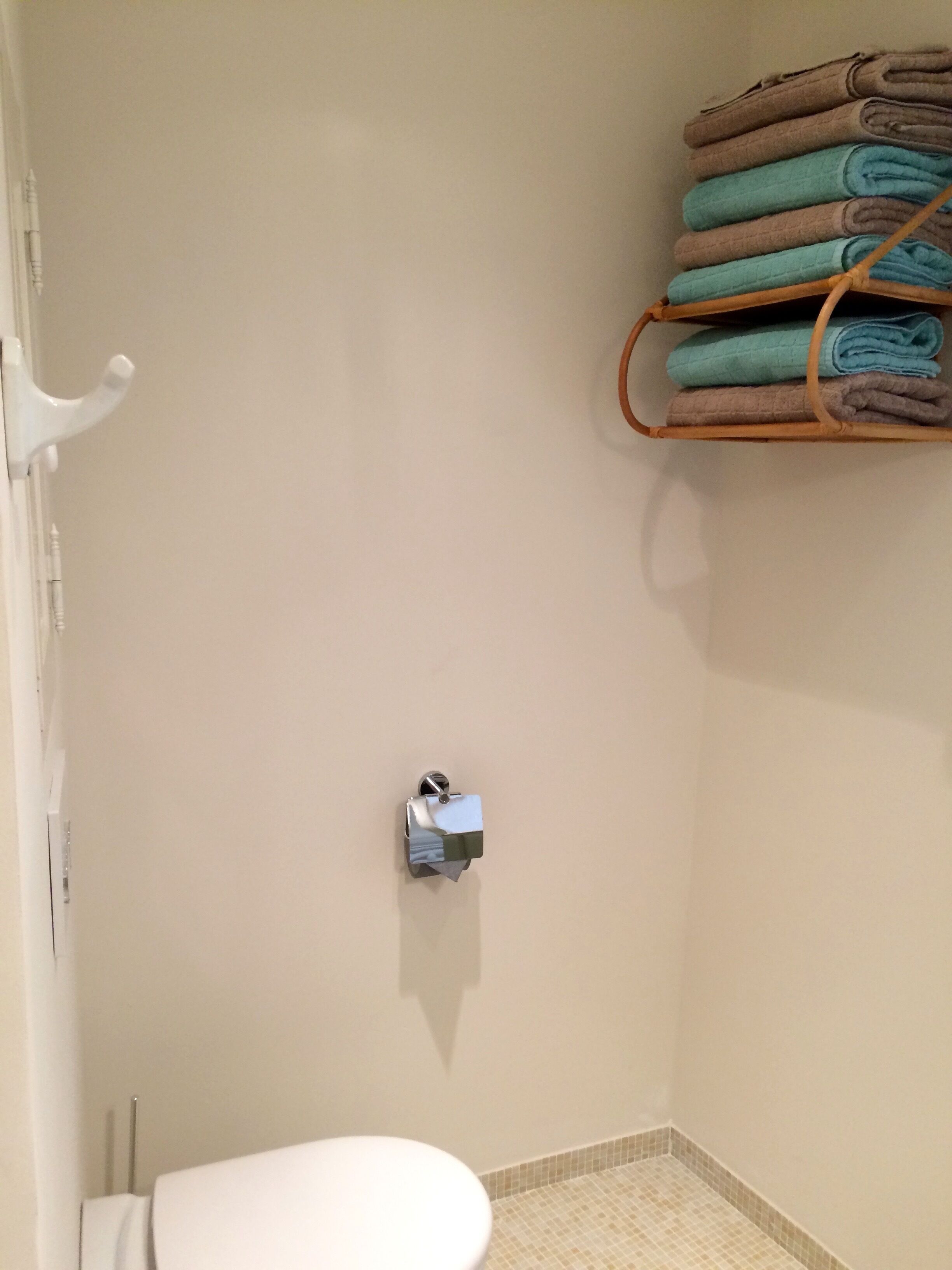 Een badkamer met een toilet, een handdoekhouder met opgevouwen handdoeken en een keukenrolhouder.