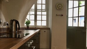 Una cucina con piano di lavoro in legno, bollitore in acciaio inossidabile e una sveglia appesa al muro.