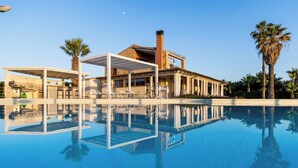 Ein Pool mit klarer Spiegelung, ein überdachter Außenbereich mit Stühlen und ein Gebäude mit Säulen.