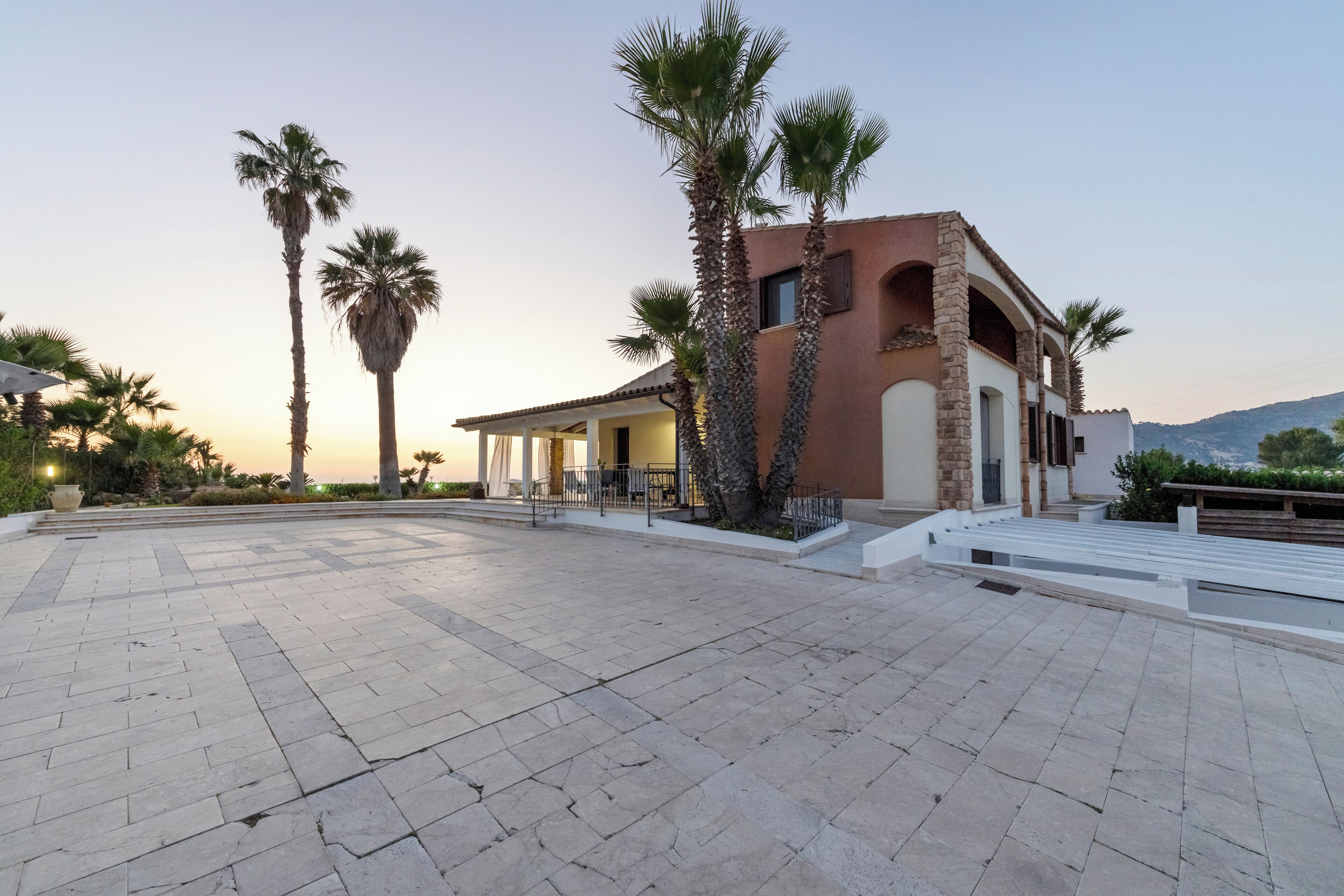 A modern building with a patio area, palm trees, and a clear sky.