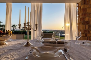 A table set for dining with a view of the sunset, a candelabra, and a bowl of fruit.