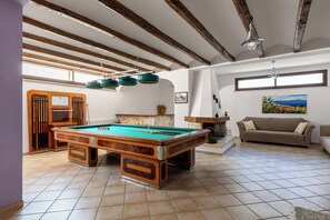 Una mesa de billar en una habitación con vigas de madera a la vista, un sofá y un cuadro en la pared.