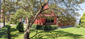 A red building with a covered porch, surrounded by well-maintained grass and bushes. - Glewitz Am Alten Fährhaus 4 (Garz/Rügen)