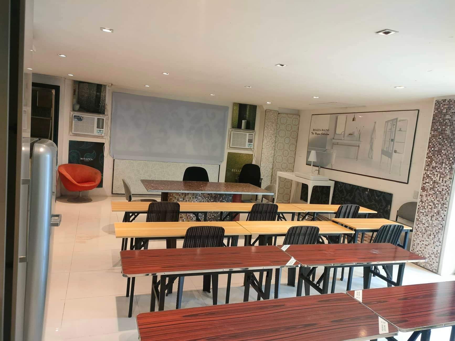 Una sala de conferencias moderna con mesas de madera y sillas negras, una silla roja, y un ventanal grande.