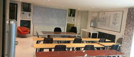 Una sala de conferencias moderna con mesas de madera y sillas negras, una silla roja, y un ventanal grande.