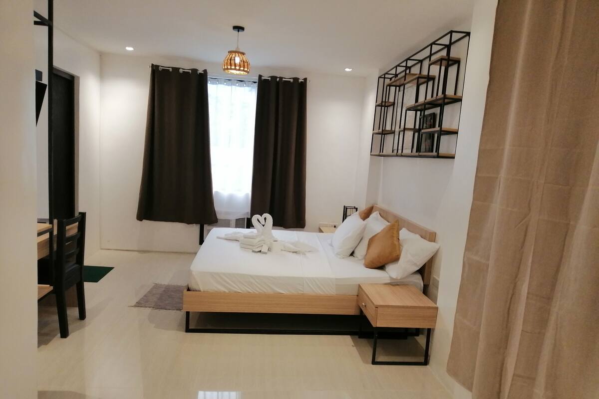 A modern hotel room with a large bed, a desk, and a bookshelf.