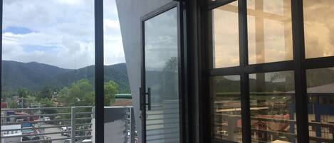 Blick vom Balkon mit Glastür auf einen Parkplatz und eine gebirgige Landschaft.