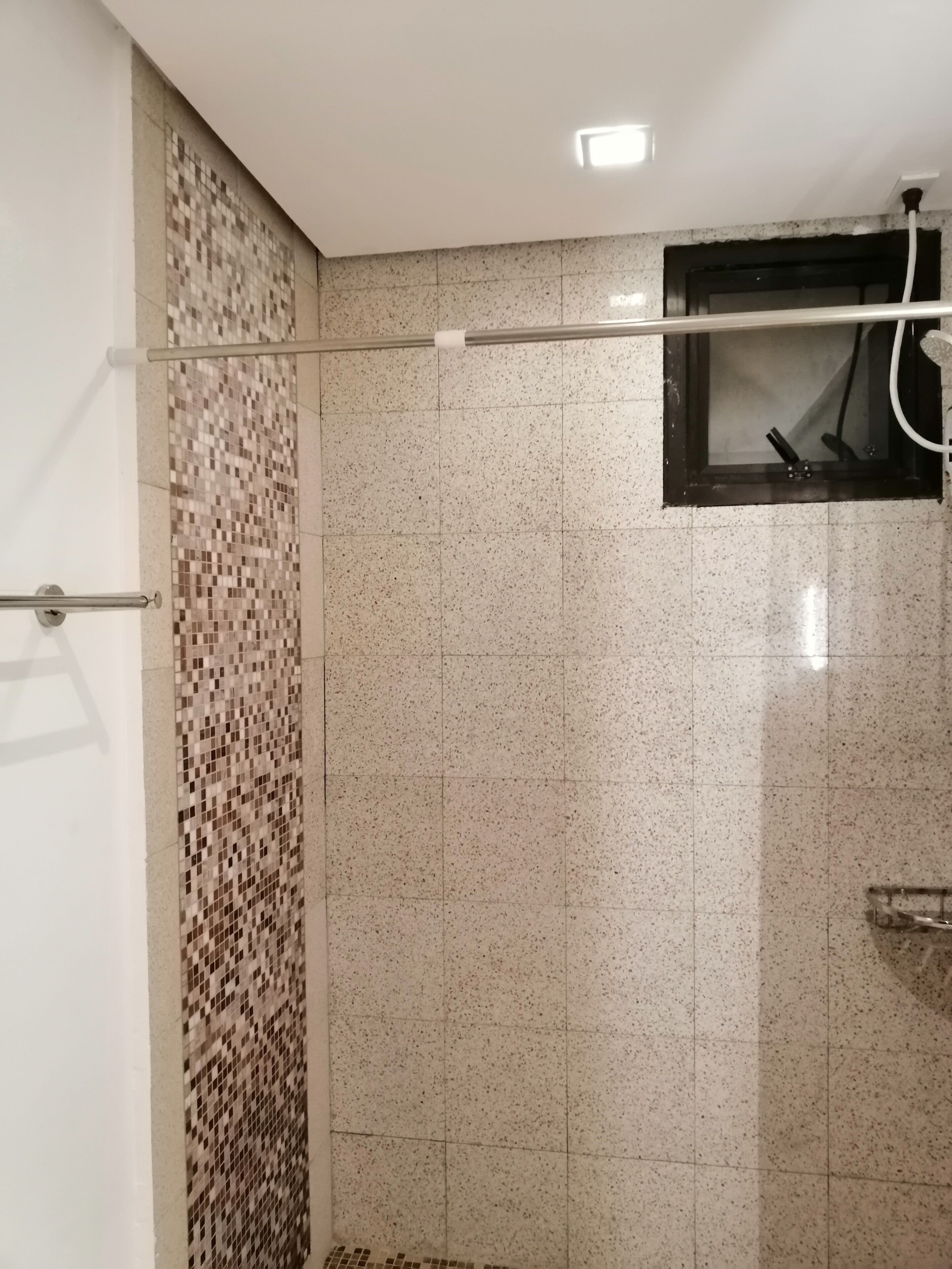 A bathroom with a shower area, tiled walls, and a window with a towel rack.