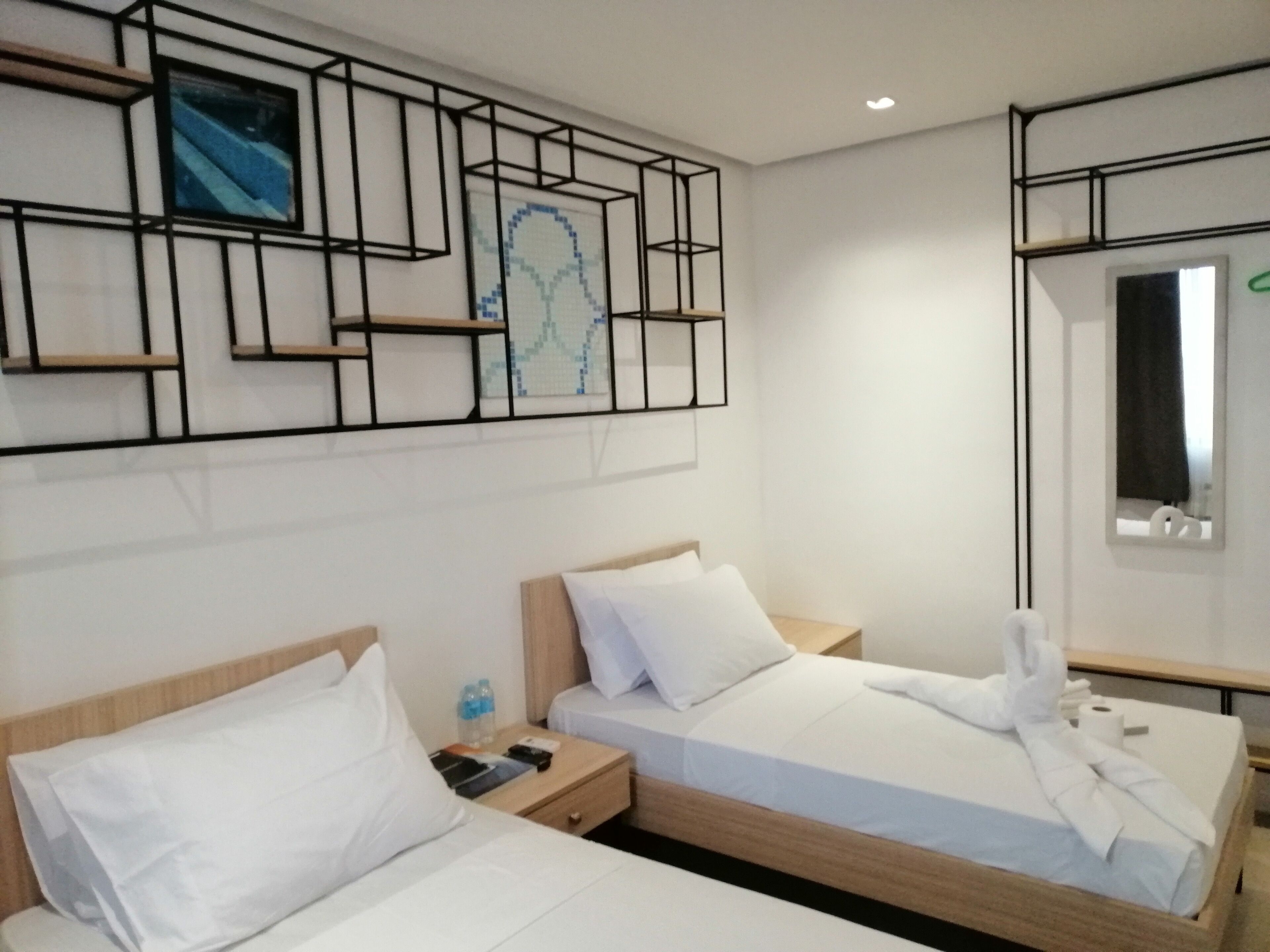 A hotel room with two beds, a nightstand, a mirror, and a wall art piece.