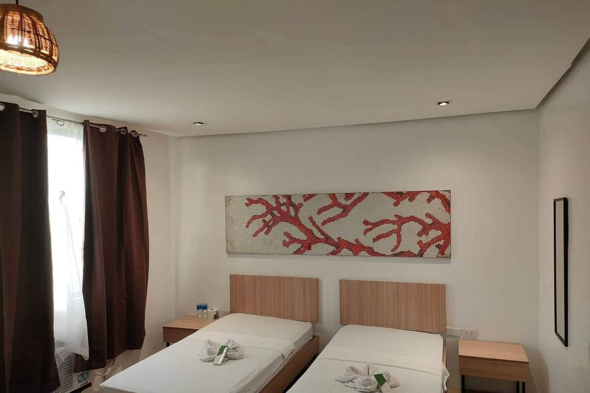 A hotel room with two beds, a large abstract artwork on the wall, a wooden headboard, a small table, and a heater.
