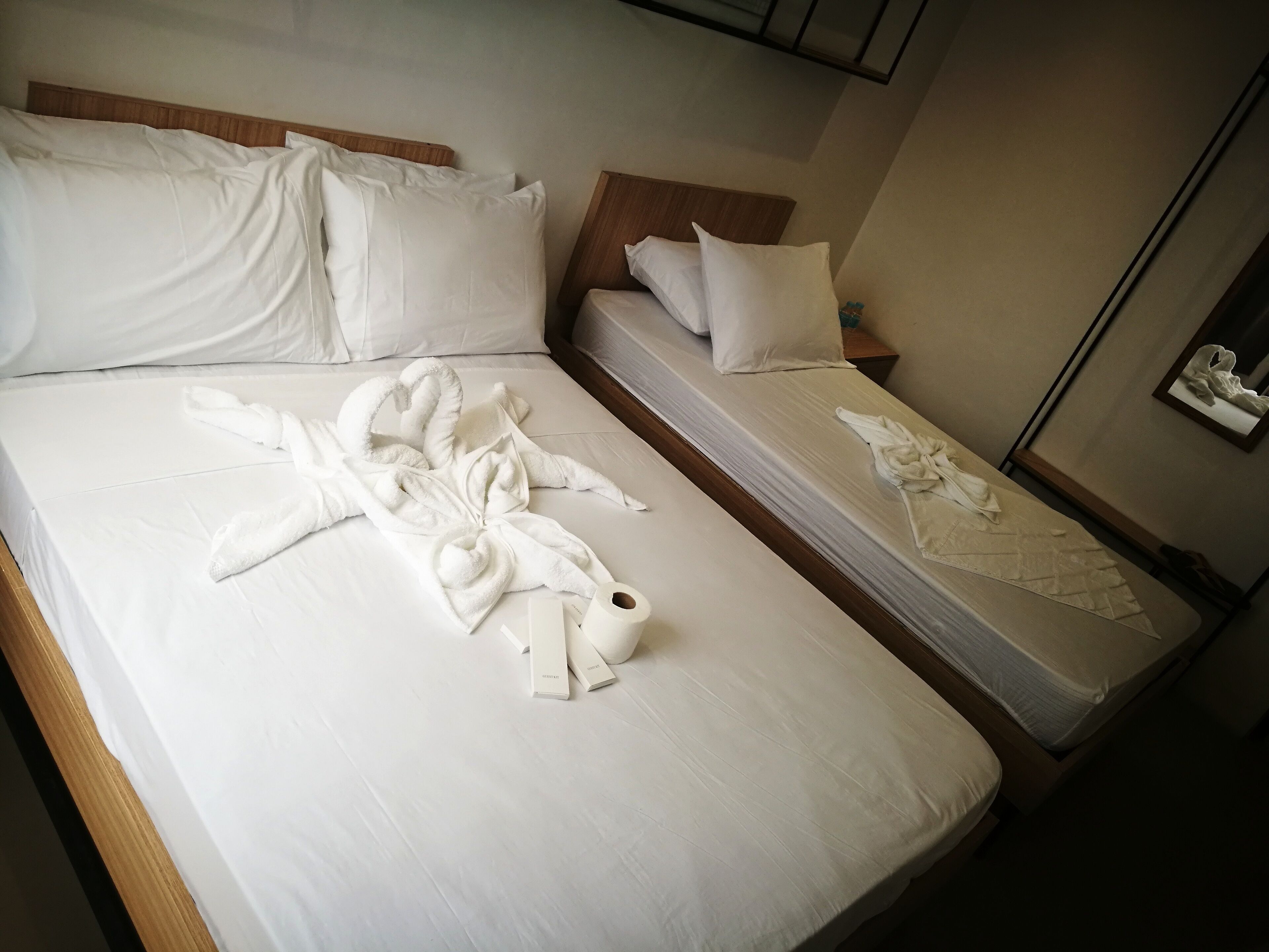 A hotel room with two beds, each with white linens and pillows. There are towels and toiletries on the beds.