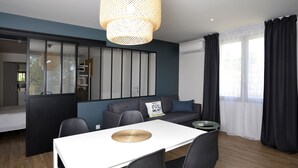 A modern living room with a sofa, a dining table with chairs, a hanging light fixture, and a large window with curtains. - CHARMING APARTMENT WITH TERRACE IN A QUIET RESIDENCE NEAR JONZAC CENTER (Jonzac)