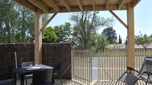 An outdoor patio with a table and chairs, a wooden pergola, and a view of a fenced area with trees and buildings in the background. - CHARMING APARTMENT WITH TERRACE IN A QUIET RESIDENCE NEAR JONZAC CENTER (Jonzac)
