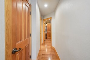 Un couloir avec des portes en bois et une cuisine visible au loin.