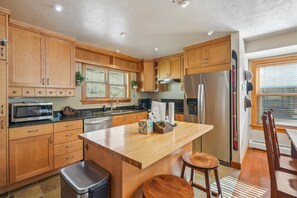 Une cuisine moderne dotée de meubles en bois, d’appareils électroménagers en acier inoxydable, d’un îlot central et d’un coin repas avec une table et des chaises en bois.