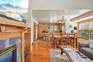 Une cuisine moderne avec des meubles en bois, un coin repas avec une table et des chaises en bois, et un salon avec un canapé et une cheminée.