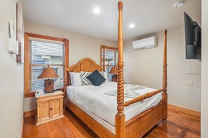 Uma cama de dossel com cabeceira de madeira, mesa de cabeceira com luminária e ar-condicionado fixado na parede.