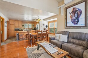 A spacious living area with a leather sofa, wooden dining table, and a kitchen in the background.