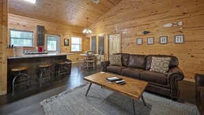 A wooden cabin interior with a living room, kitchen, and dining area. - Firefly at Lazy River Cabins on Mt Fork River (Broken Bow)