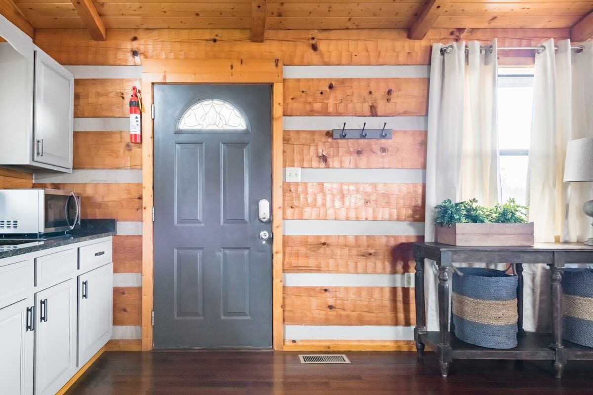 A wooden interior with a door, cabinets, a microwave, a plant, and a table with baskets.