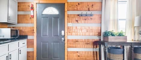 Interior de madera con una puerta, armarios, un microondas, una planta y una mesa con cestas.
