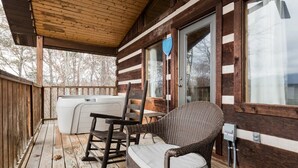 A wooden cabin with a porch, a hot tub, wicker chairs, and a window with a blue shield. - Amazing Mt. LeConte Views/Gatlinburg Log Cabin (Gatlinburg)
