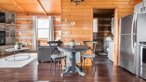 A wooden interior with a round dining table, chairs, a chandelier, and a kitchen area with stainless steel appliances. - Amazing Mt. LeConte Views/Gatlinburg Log Cabin (Gatlinburg)