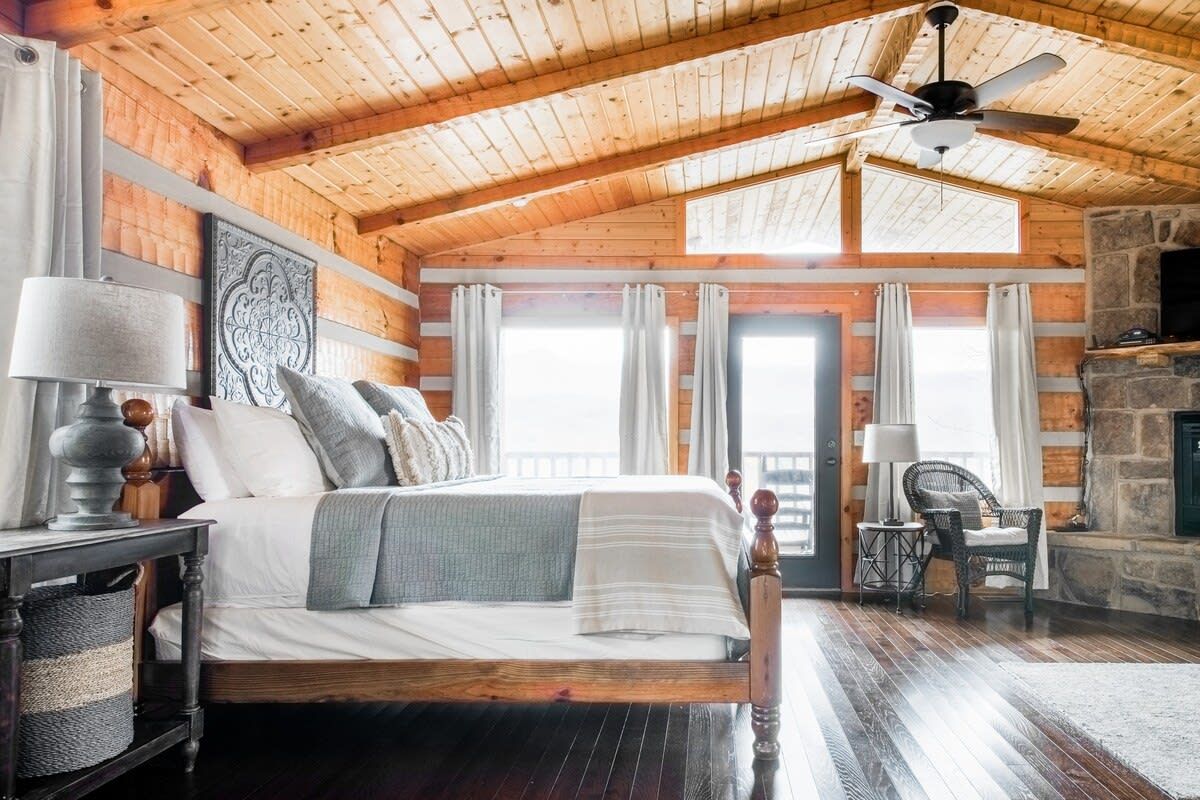 A wooden cabin bedroom with a bed, a fireplace, and a ceiling fan.