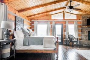 Une chambre dans une cabane en bois, avec un lit, une cheminée et un ventilateur de plafond.
