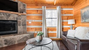 A cozy cabin interior with a stone fireplace, a round table with a plant, a leather sofa, and a painting on the wall. - Amazing Mt. LeConte Views/Gatlinburg Log Cabin (Gatlinburg)