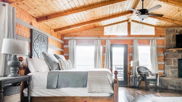 A cozy log cabin bedroom with a large bed, a stone fireplace, and a ceiling fan. - Amazing Mt. LeConte Views/Gatlinburg Log Cabin (Gatlinburg)