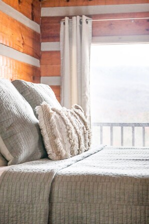 A bed with a quilted bedspread and two pillows, a knitted throw, and a view of a wooden balcony railing. - Amazing Mt. LeConte Views/Gatlinburg Log Cabin (Gatlinburg)