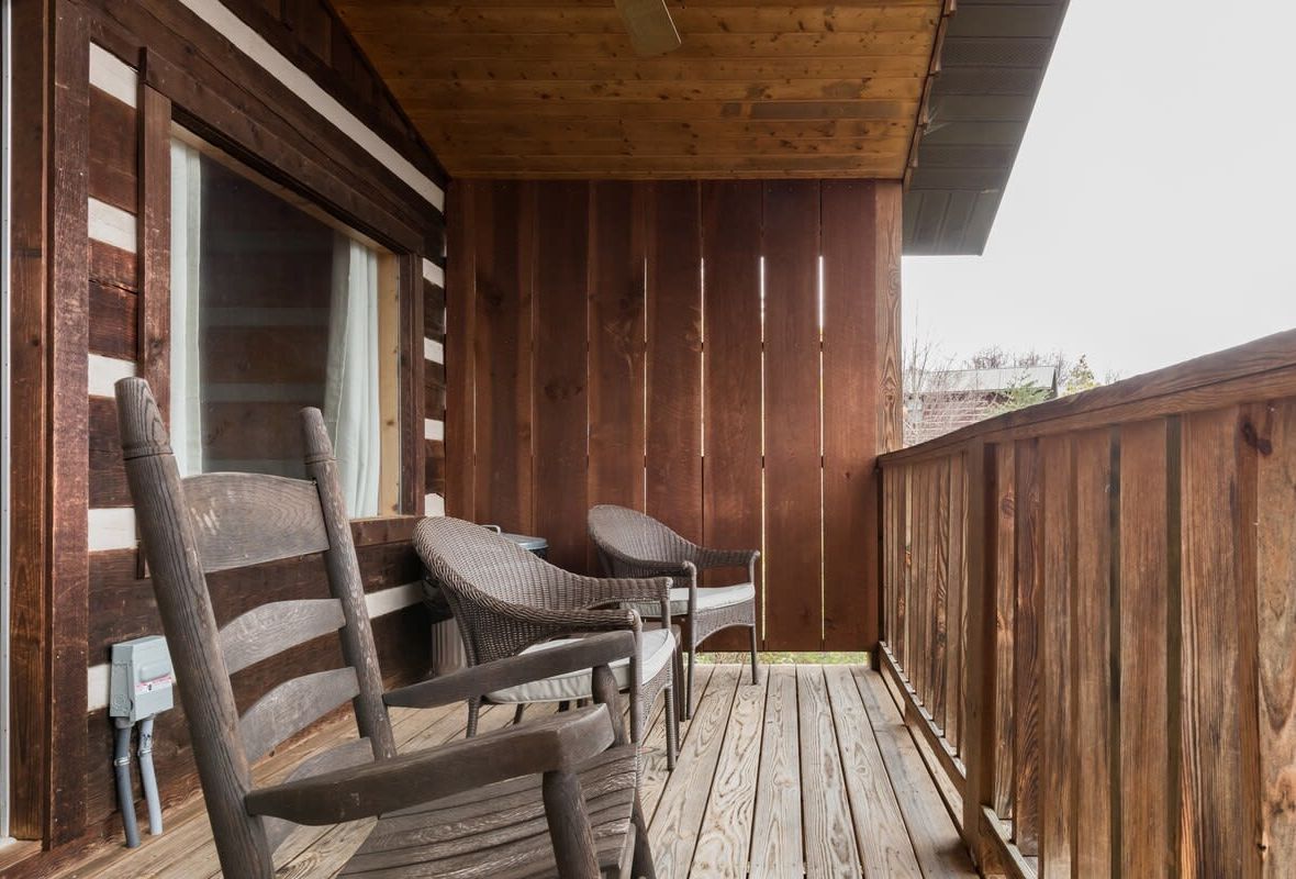 A wooden deck with two wicker chairs and a window.
