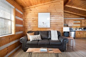 A cozy cabin interior with a wooden interior, a leather sofa, a coffee table, and a kitchen area. - Gigantic Views GSMNP/3.6 Miles 2 DwTn Gatlinburg (Gatlinburg)