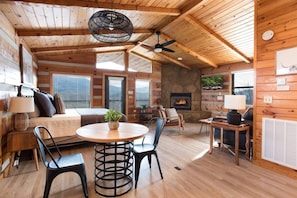 Een gezellig chaletinterieur met een houten plafond, een open haard, een ronde eettafel en een comfortabele zithoek.